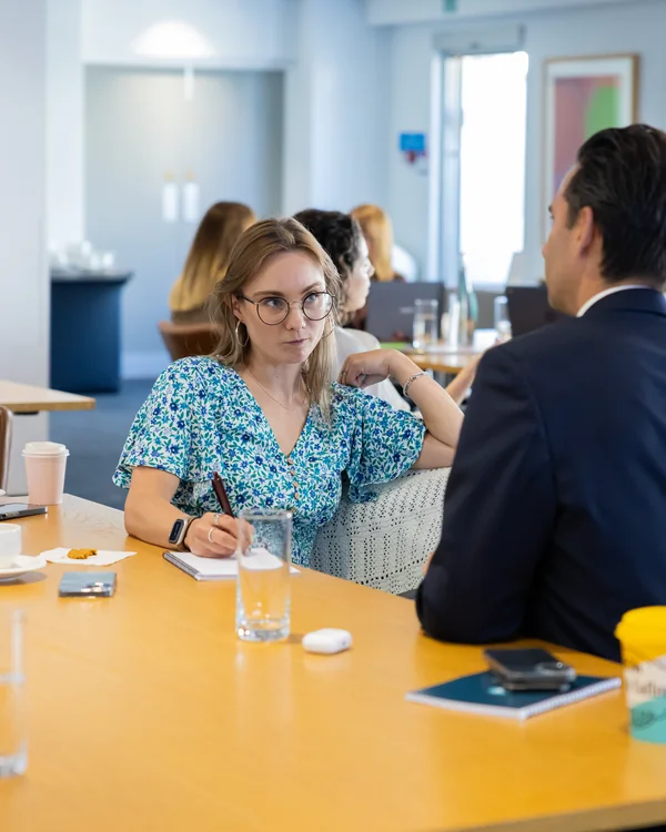 Two people in conversation across a table during an LCG training session, one taking notes.